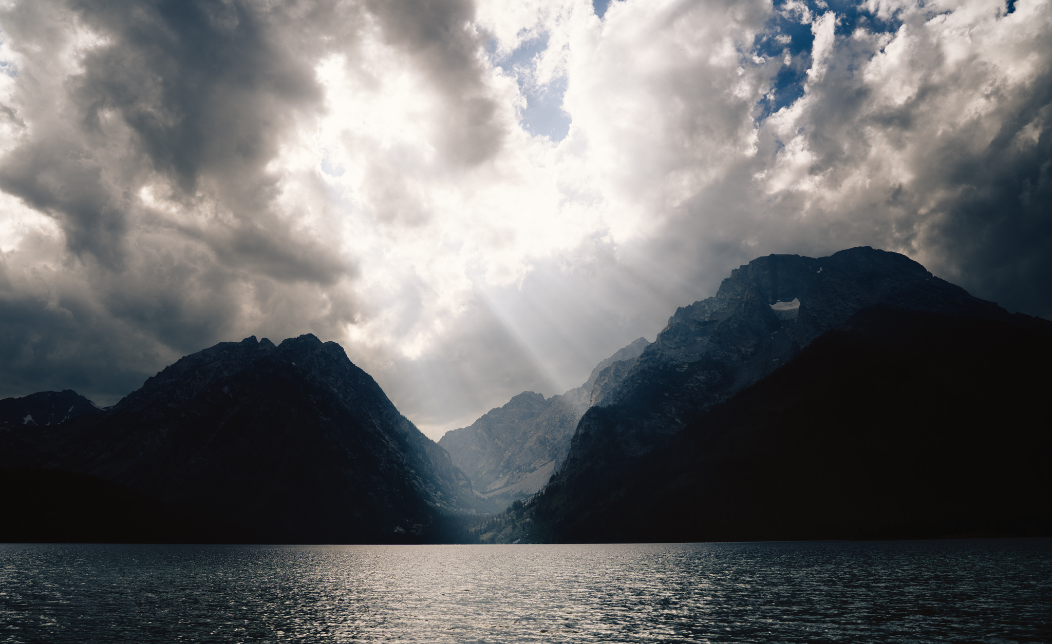 Sunbeams breaking through storm clouds over a mountain lake